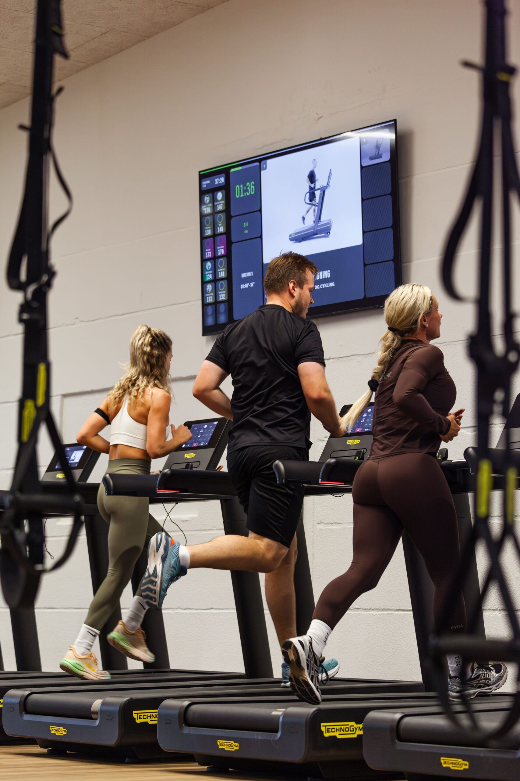 Tre personer løber på Technogym løbebånd til holdtræning med pulstracking hos Performance Klubben i Højbjerg.