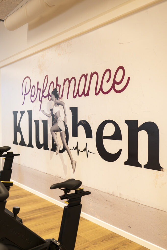 Indretning i Performance Klubben med motionscykler og vægdekoration i træningscenteret i Højbjerg.